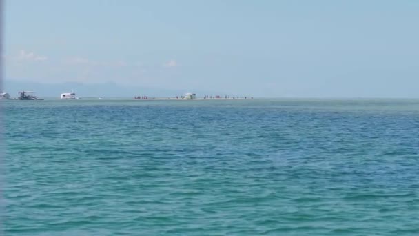 Uitzicht vanaf de boot op het eiland in de tropen met mensen, jachten en zandstrand. — Stockvideo