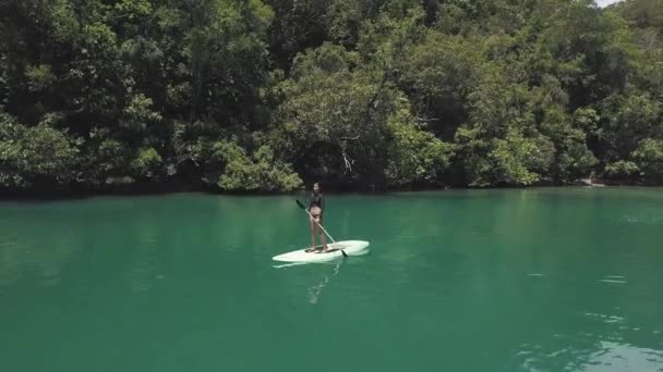 Beautiful woman paddleboarding in a serene lagoon in Asia, drone view. — Stock Video