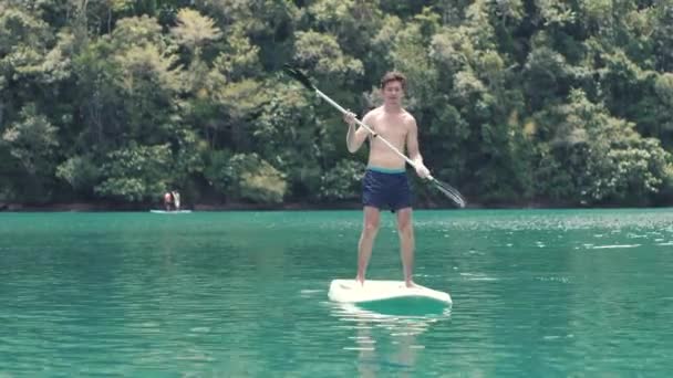 Ein gutaussehender Typ tanzt auf einem Stand Up Paddle Board und genießt den Sommerurlaub — Stockvideo