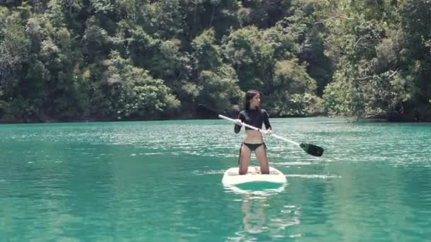 Beautiful Asian woman enjoy paddleboarding in a turquoise green water of lagoon. — Stock Video