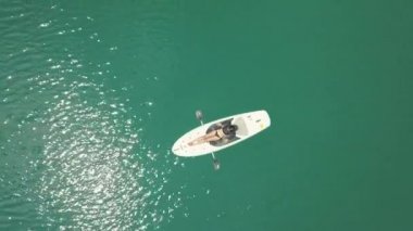 Drone görünümü: Asyalı kız tatilde, sakin denizde bir paddleboard üzerinde yatan.