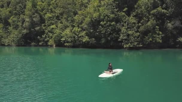 En flicka som sitter på paddelbräda, stretching händer, koppla av i en fredlig lagun. — Stockvideo