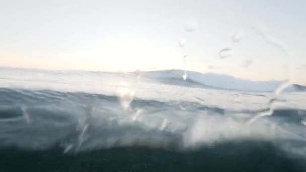 Vista submarina de las olas del océano azul con burbujas de agua brillando contra el amanecer . — Vídeos de Stock