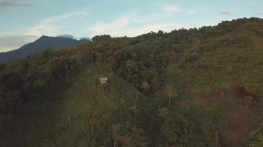 Drone flyover küçük evler, mavi gökyüzü ve dağlar ile tropikal yeşil orman.
