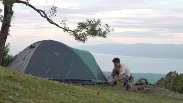 Caucásico chico montando tienda de campaña en la colina de la montaña con espectacular vista natural — Vídeos de Stock