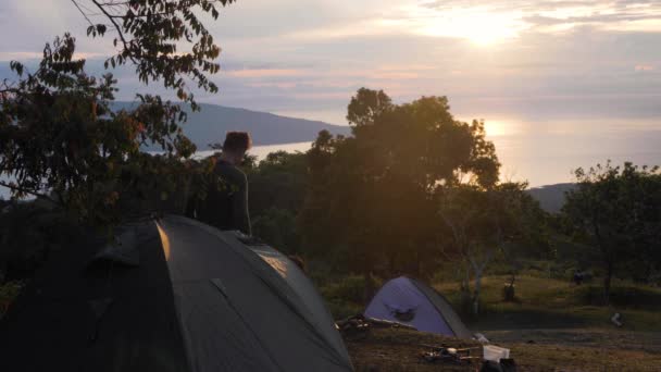 Um jovem sai da tenda de acampamento e faz alongamento ao nascer do sol . — Vídeo de Stock