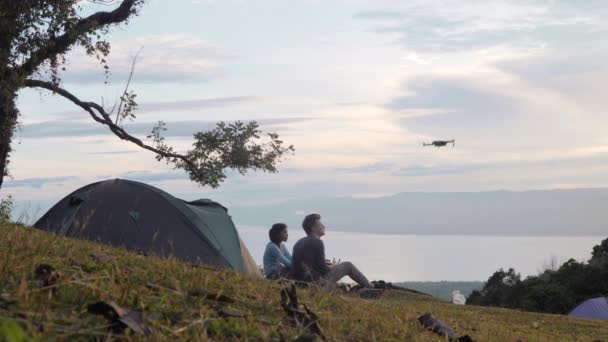 Fiatal pár kemping természettel ül a fűben, és repül a drone. — Stock videók