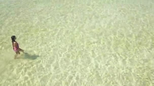 Top side view of a tourist in one piece swimwear walking in crystal clear water. — Stock Video