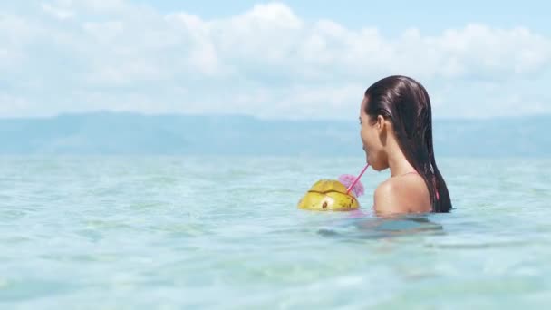 Mujer joven relajándose en el océano bebe jugo de coco en agua clara del océano . — Vídeos de Stock