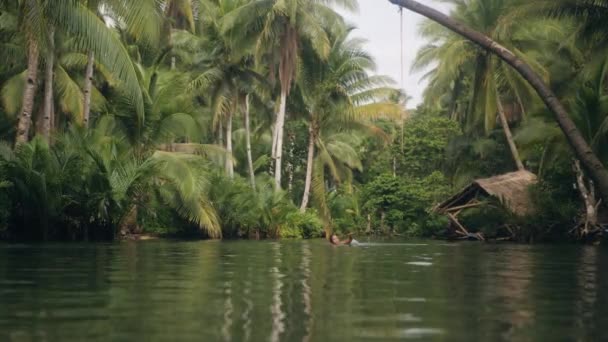 En kvinna simmar i en flod soravrundad av tropiska lövverk. — Stockvideo