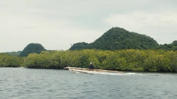 En man på en liten båt som seglar över lugnt hav nära mangroveträsk och vackra kullar — Stockvideo