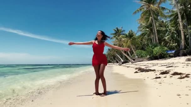 Glücklich tanzende junge Frau, die sich barfuß in einem roten Kleid am Strand dreht — Stockvideo