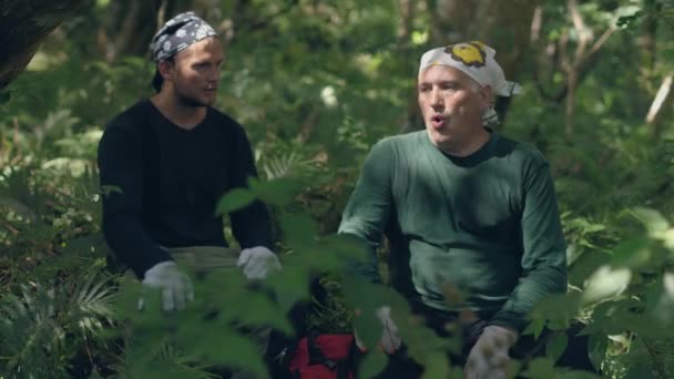 Два туриста отдыхают, сидя в лесу и разговаривая друг с другом . — стоковое видео