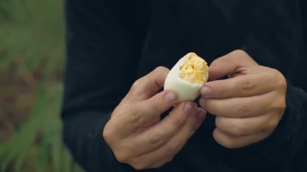 Man tourist peeling and eating boiled egg sitting in forest camping. — Stock Video