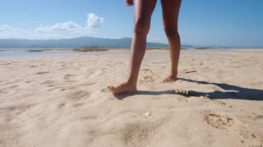 Sahilde yürüyen bir çift kadının bacağı kumda ayak izleri bırakarak.