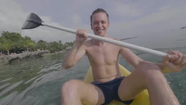 Lächelnder junger Mann glücklich beim Kajakfahren im Meer auf einer tropischen Insel im Sommer — Stockvideo