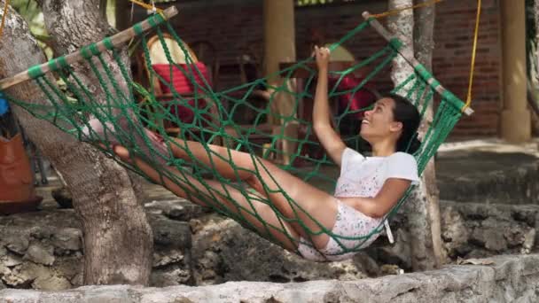 Joven mujer asiática alegre que relaja en la hamaca con una sonrisa en su cara . — Vídeos de Stock