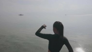 Güneşli bir günde kıyı kenarında egzersiz yapan ince bir kadının arka görüntüsü..