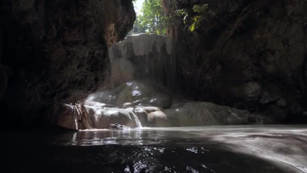 Barlang vízesés egy sziklás fal a víz csepegő és áramló ellen napfény. — Stock videók