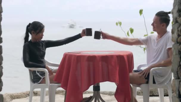 Young couple on honeymoon drinking coffee at the cafe table with ocean view. — Stock Video