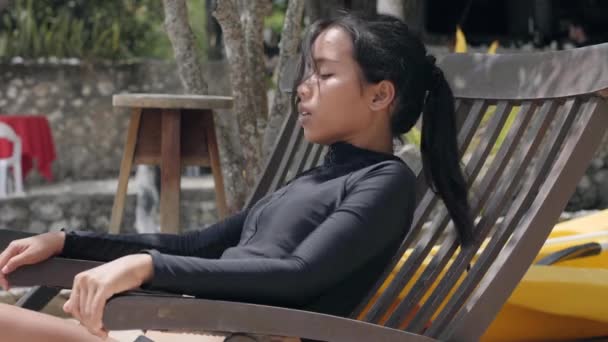 En vacker kvinna som kopplar av på stolen och njuter av den friska luften på en tropisk semesterort — Stockvideo