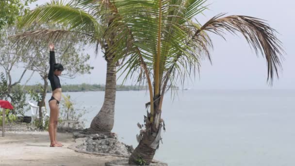 Slender woman doing warm up exercise in front of the ocean in a tropical resort. — Stock Video