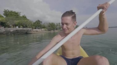 Yakışıklı genç adam tropik tatil köyünün yanındaki denizde kayak yapmaktan hoşlanıyor..