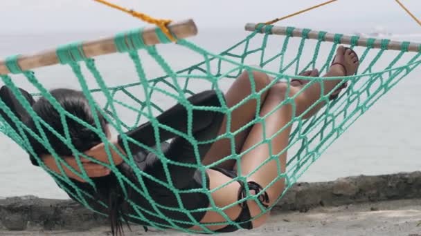 Tan mujer de piel tendida en una hamaca verde frente al mar tranquilo . — Vídeo de stock