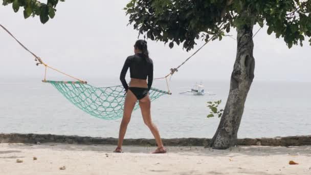 Mulher morena em uma roupa de banho sexy descansando em uma rede pendurada na praia . — Vídeo de Stock