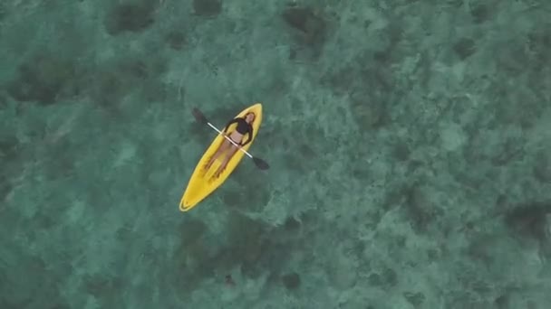 Luchtbeelden: Een vrouwelijke kajak liggend op een gele kajak in de oceaan in de zomer — Stockvideo