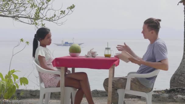 Mann und Frau sitzen an einem Tisch und unterhalten sich in einem Café am Meer. — Stockvideo