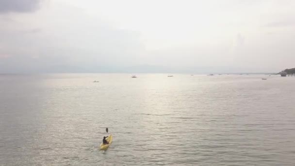 Vue aérienne : Une femme faisant du kayak dans l'océan serein avec de petits bateaux . — Video