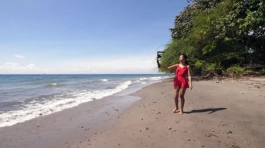 Sahilde yürüyen ve video için selfie kaydeden bir kadın vlogger..