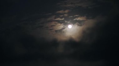 Gece gökyüzünde görünen beyaz bulutlarla dolu gerçek zamanlı bir dolunay görüntüsü..