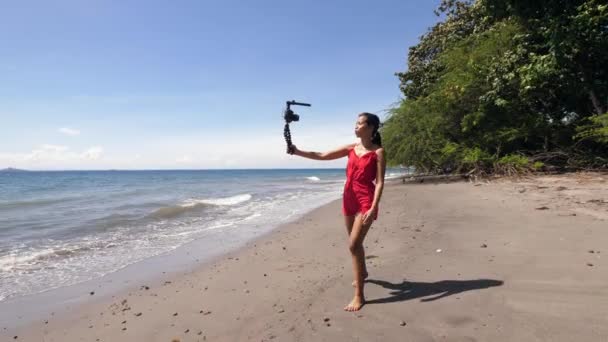 Joven influenciador milenario de las redes sociales caminando por la playa y filmando video . — Vídeos de Stock