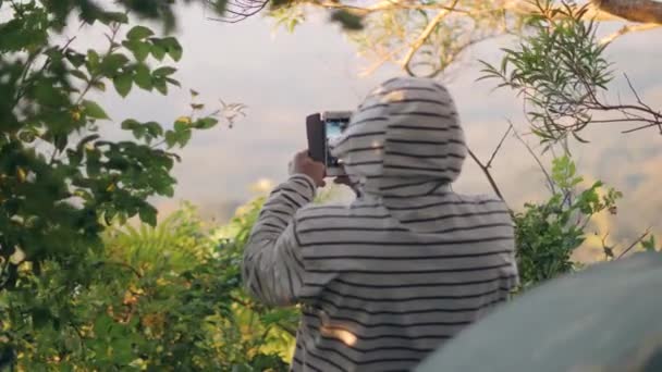 Vista trasera de un hombre en pico usando chaqueta encapuchada tomando video con un teléfono inteligente . — Vídeos de Stock