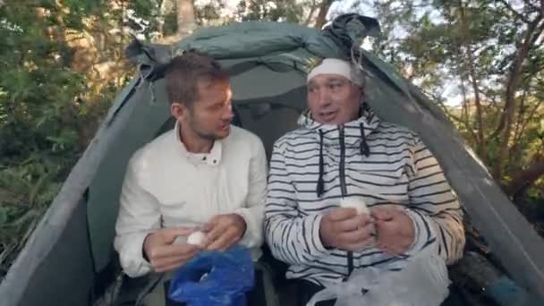 Far och son äter kokta ägg i campingtältet. — Stockvideo