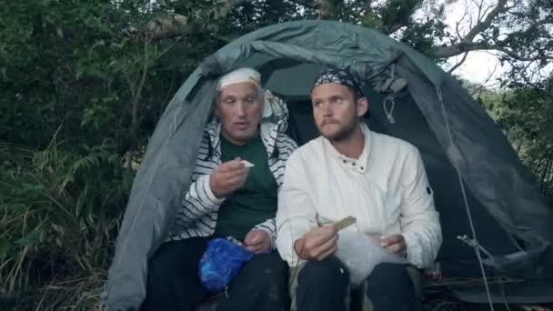 Dois campistas comendo seus lanches dentro de uma tenda de acampamento . — Vídeo de Stock