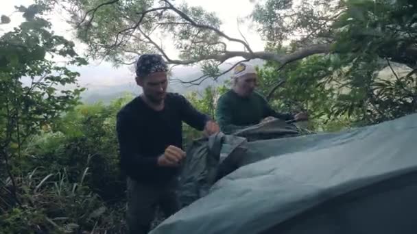 Dos campistas hombres instalan tienda en el campamento forestal para descansar en unidad con la naturaleza . — Vídeos de Stock