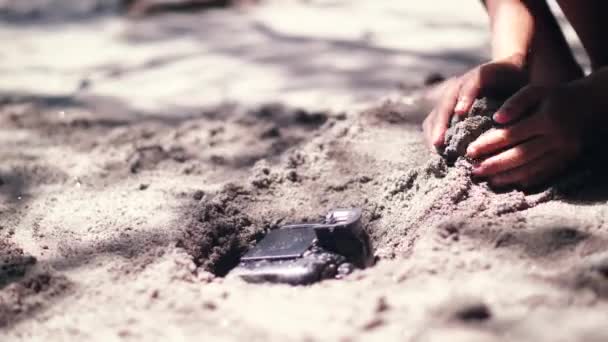 Une jeune femme enterre à la main un appareil photo numérique dans le sable . — Video