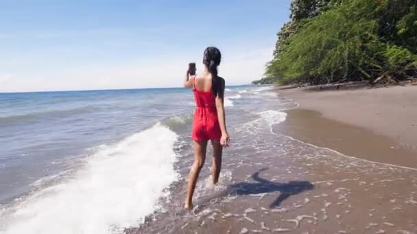 Путешествующая женщина-видеоблогер гуляет по пляжу и записывает видео на смартфон . — стоковое видео