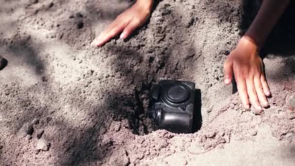 Uma jovem mulher enterrando uma câmera DSLR na areia . — Vídeo de Stock
