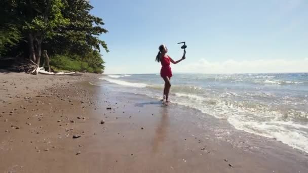 Миллениальный видеоблогер, гуляющий по пляжу и записывающий видео для социальных сетей — стоковое видео