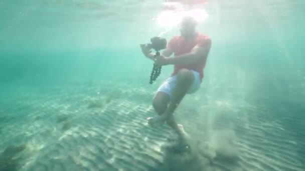 A caucasian man holding a DSLR camera with tripod filming underwater. — Stock Video