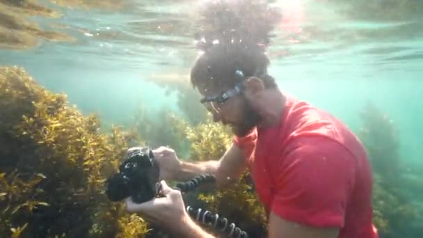 Biały mężczyzna trzymający kamerę Dslr ze statywem pod wodą. — Wideo stockowe