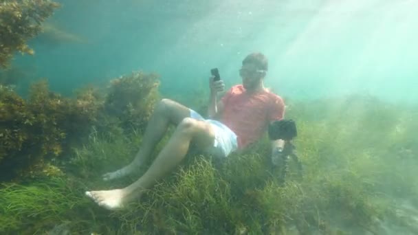 Vreemde kerel met telefoon en digitale camera onder de oceaan. — Stockvideo