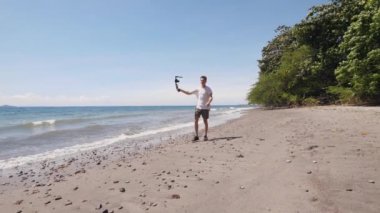 Beyaz bir erkek vlogger sahilde yürüyor ve selfie videosu çekiyor..