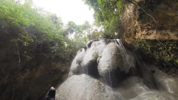 Mujer sexy de pie debajo de una cascada disfruta viendo el agua mientras cae — Vídeos de Stock