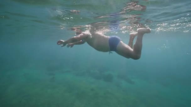 Underwater view of senior man in snorkeling mask diving into the sandy seabed. — Stock Video