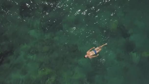 Luftaufnahme eines sexy jungen Mannes in blauen Badehosen, der schwimmt und im Ozean treibt — Stockvideo